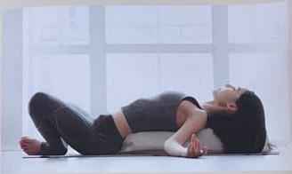 Frau in entspannter Rückenlage auf einem Bolster beim Restorative Yoga